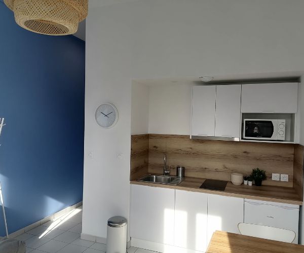 Cuisine rénovée d’un studio à Marseille avec meubles blancs et crédence bois